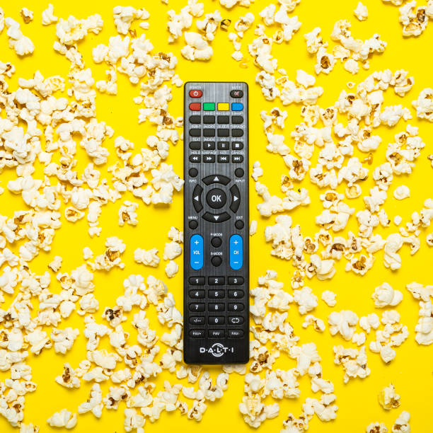istock Black remote control from a TV, TV tuner or audio system on a yellow background with popcorn. Concept TV series, film, sports. Flat lay, top view 1270499045