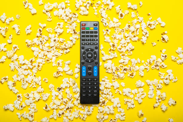 istock Black remote control from a TV, TV tuner or audio system on a yellow background with popcorn. Concept TV series, film, sports. Flat lay, top view 1270499997