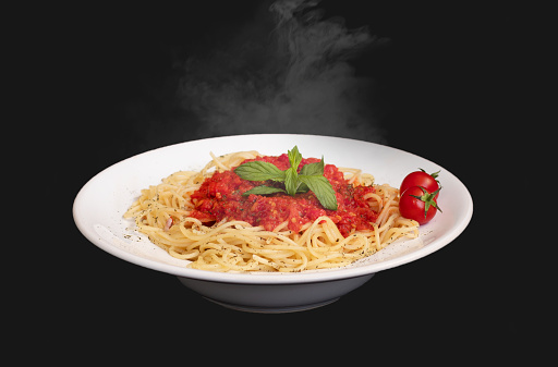 Hot pasta with steaming on dark background. Pasta served with spicy tomato sauce on black background. Hot food concept.