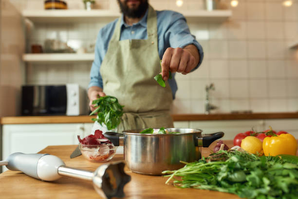 istock Cropped shot of man, chef cook adding basil leaf to the pot with chopped vegetables while preparing healthy meal, soup in the kitchen. Cooking at home, Italian cuisine concept 1270506844