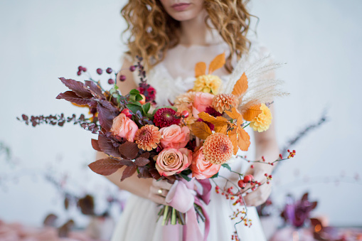 Bride holds beautiful autumn bouquet with orange and red flowers and berries. Autumn bouquet with ribbons in bride's hands