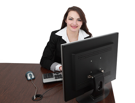 Image of a young woman in front of a computer at her workplace looking to the camera and smiling, isolated against a white background.