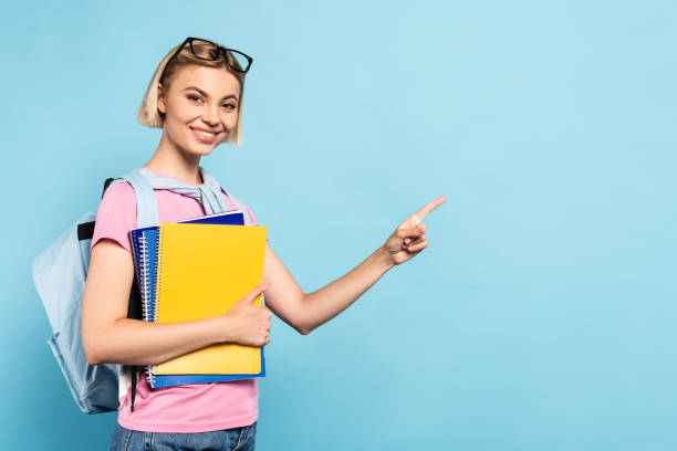istock young blonde student with backpack holding notebooks and ponging with finger on blue 1270533053
