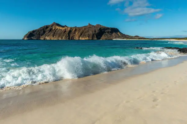 Landscape of strong waves by the beach in Stephens Bay with Witch Hill in the background, San Cristobal island, Galapagos, Ecuador.