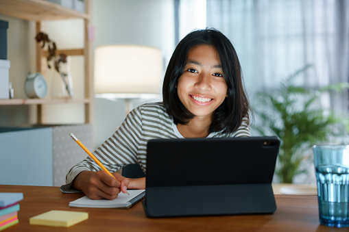 La educación en casa chica asiática haciendo la tarea y estudiar en línea con la tableta en la noche de escritorio. Retrato de la felicidad infantil de Asia y confianza sonriente mirando a la cámara photo