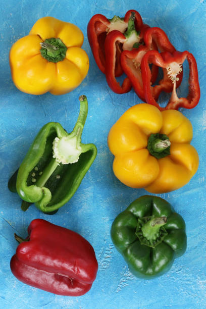 imagen de filas enteras, cortadas a la mitad y cortadas en rodajas, pimientos mixtos, rojo, verde y amarillo sobre fondo azul turquesa, concepto de alimentación saludable, vista elevada - chopped green bell pepper pepper bell pepper fotografías e imágenes de stock