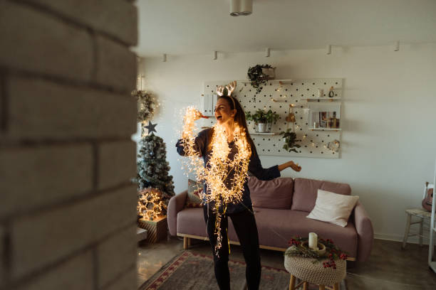 Having my solo concert in the living room Photo of an excited young woman singing while decorating the living room of her apartment; wrapped in Christmas lights and wearing shiny reindeer antlers; preparing for the upcoming holidays. making music stock pictures, royalty-free photos & images