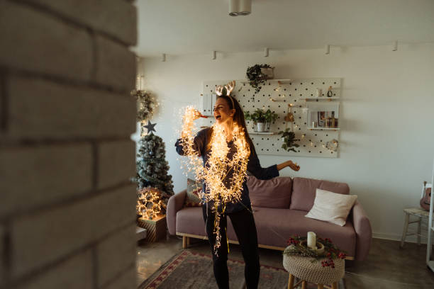 Having my solo concert in the living room Photo of an excited young woman singing while decorating the living room of her apartment; wrapped in Christmas lights and wearing shiny reindeer antlers; preparing for the upcoming holidays. christmas excitement stock pictures, royalty-free photos & images