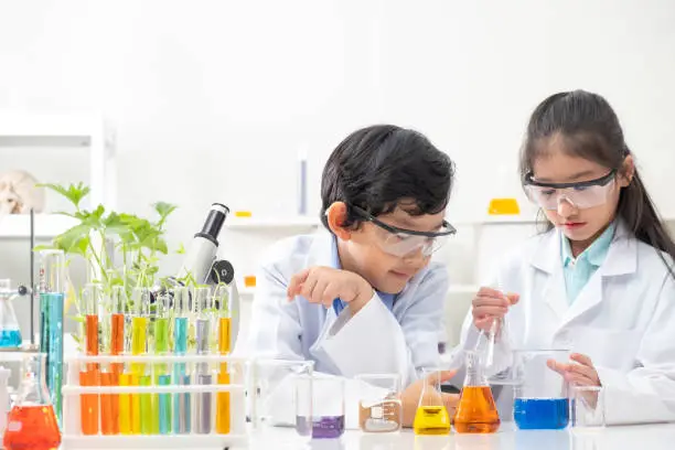 Young Asian boy and girl smile and having fun while learning science experiment in laboratory with teacher in classroom. Study with scientific equipment and tubes. Education concept.