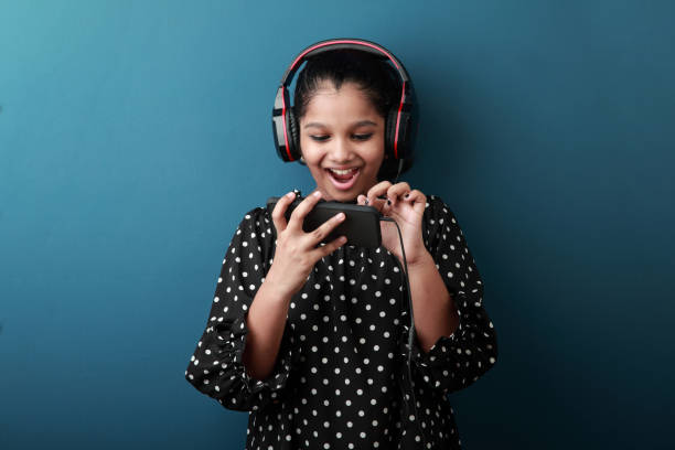 jovem animada usando conjunto de cabeça engajado com um telefone inteligente - indian girls audio - fotografias e filmes do acervo