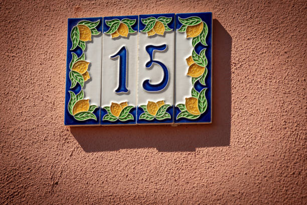House Number 15 on the wall - Liguria Italy Close-up of house number 15 (fifteen), made of ceramic, on the red wall in a small village. Liguria, Italy, Europe ceramic tile house numbers stock pictures, royalty-free photos & images