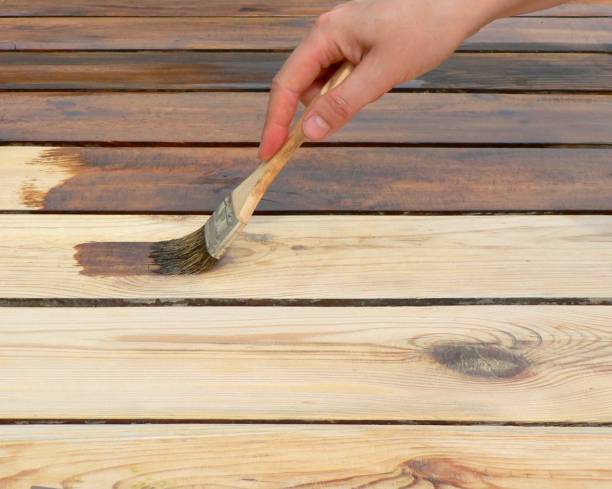 istock Hand holding a brush applying varnish paint on a wooden surface. Board half painted. Applying a protective varnish to a wooden board, table or floor. 1270580069
