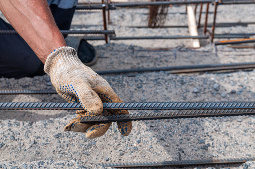 A man's hand in work gloves holds a rebar