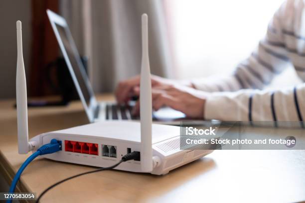 Selective Focus At Router Internet Router On Working Table With Blurred Man Connect The Cable At The Background Fast And High Speed Internet Connection From Fiber Line With Lan Cable Connection Stock Photo - Download Image Now