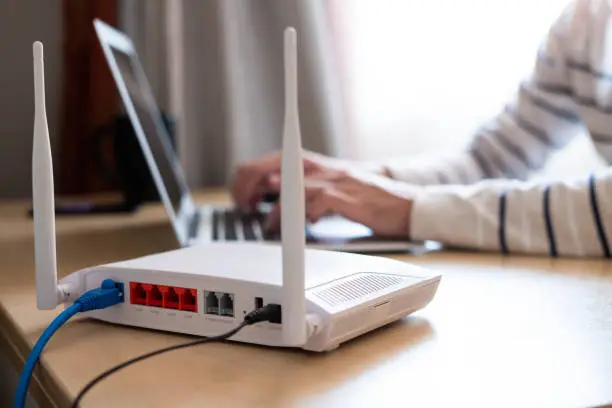 Photo of Selective focus at router. Internet router on working table with blurred man connect the cable at the background. Fast and high speed internet connection from fiber line with LAN cable connection.
