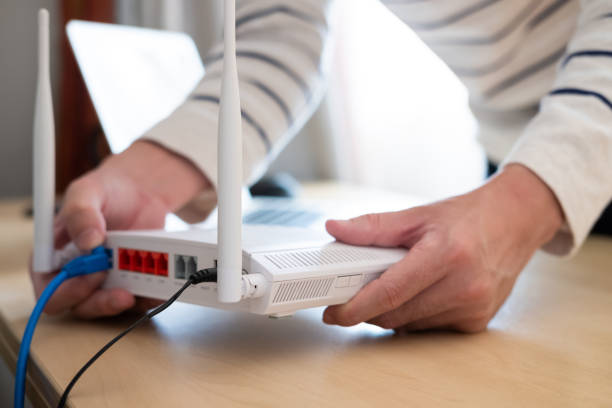 istock Selective focus at router. Internet router on working table with blurred man connect the cable at the background. Fast and high speed internet connection from fiber line with LAN cable connection. 1270583067