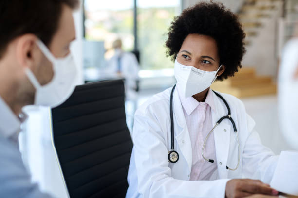 African American doctor wearing protective face mask while talking to a patient at clinic. Black female doctor communicating with a patient while wearing protective face mask during medical appointment. kn95 face mask photos stock pictures, royalty-free photos & images