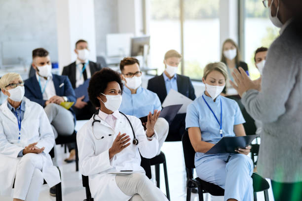 Happy African American doctor talking to a presenter while attending a seminar during coronavirus epidemic. Happy black healthcare worker wearing protective face mask communicating with a businessman who is holding educational event at convention center. business conference photos stock pictures, royalty-free photos & images