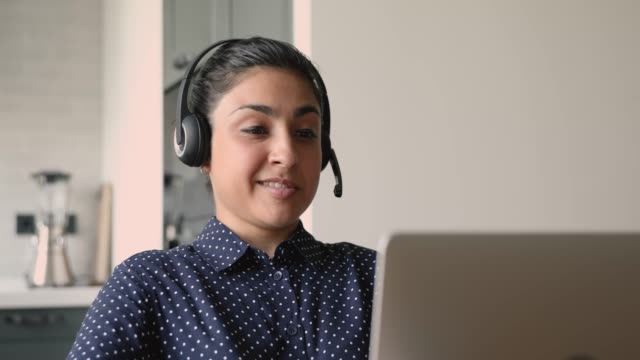 Indian businesswoman wear headset communicates distantly use laptop videocall app