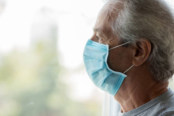 istock Old man with medical face mask looking through window 1270587688