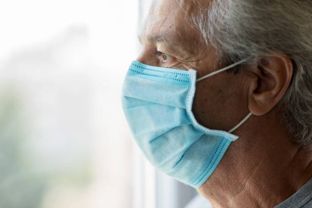 istock Old man with medical face mask looking through window 1270587777