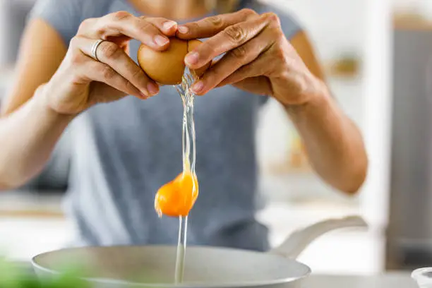 Close up of unrecognizable woman cracking an egg into a bowl.