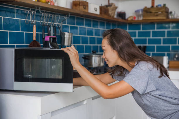Beautiful Asian woman reheating her meals inside microwave. stock photo