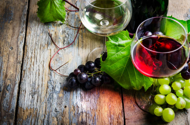 красное и белое вино в бокалах с виноградом на деревянном столе - wine cork white wine grape стоковые фото и изображения