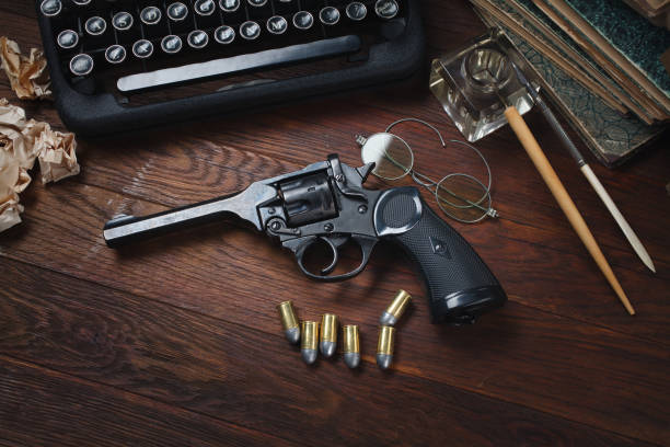 istock Crime fiction story - old retro vintage typewriter and revolver gun with ammunitions, books, blank paper, old ink pen 1270593473