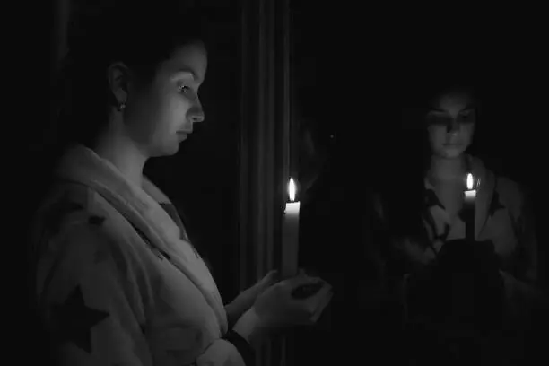 Photo of Black and white girl in a dark room with a candle in her hand in front of the mirror