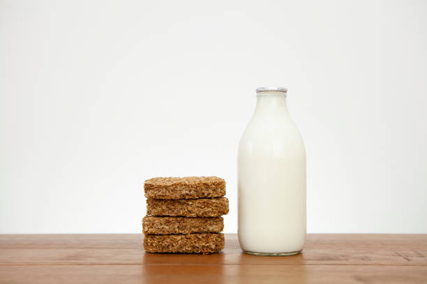 Stack of 4 Weetabix breakfast cereal biscuits next to a pint of milk on a wooden surface with copy space Four breakfast cereal biscuits stacked on top of each other next to a full pint of milk on a wooden table against a light coloured wall. Part of a series. weetabix with milk stock pictures, royalty-free photos & images
