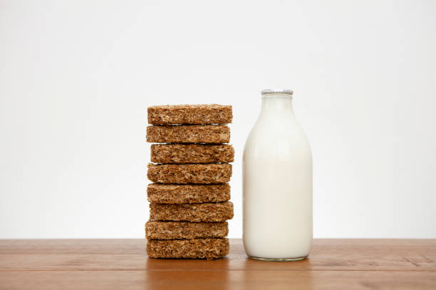 Stack of 8 Weetabix breakfast cereal biscuits next to a pint of milk on a wooden surface with copy space Eight breakfast cereal biscuits stacked on top of each other next to a full pint of milk on a wooden table against a light coloured wall. Part of a series. weetabix with milk stock pictures, royalty-free photos & images