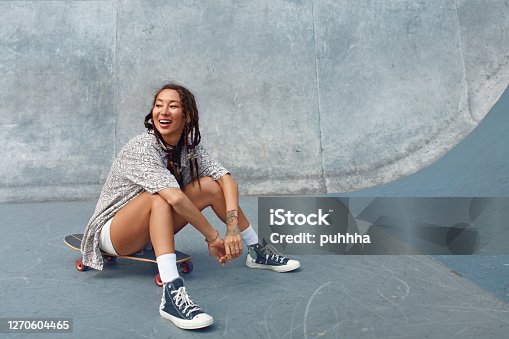 istock Portrait Of Skater Girl In Skatepark. Female Teenager In Casual Outfit Sitting On Skateboard Against Concrete Wall. Summer Skateboarding With Modern Sport Equipment As Part Of Active Lifestyle. 1270604465