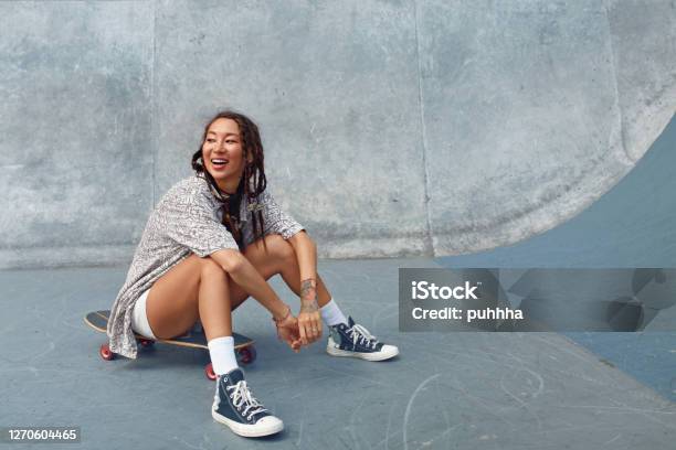 Portrait Of Skater Girl In Skatepark Female Teenager In Casual Outfit Sitting On Skateboard Against Concrete Wall Summer Skateboarding With Modern Sport Equipment As Part Of Active Lifestyle Stock Photo - Download Image Now