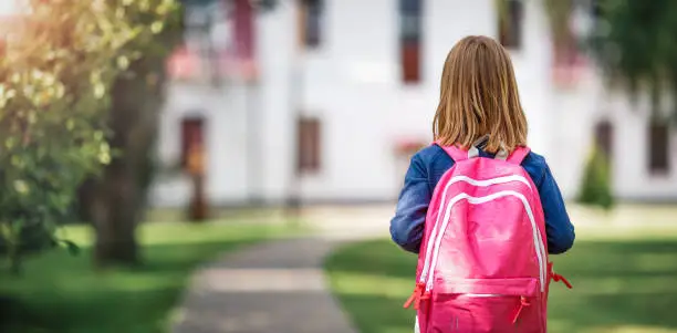 Photo of Girl with rucksack in front of a school building