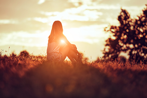Silhouette of a woman sitting on a field.