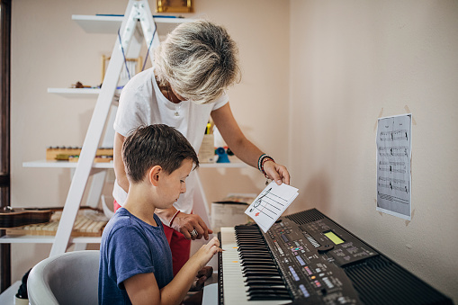 Two people, young boy on piano class with female teacher, learning to play piano.