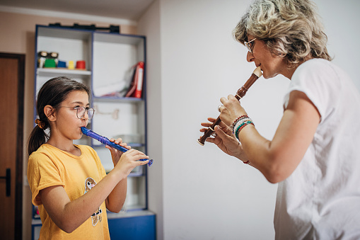Two people, young girl on music class with female teacher, learning to play flute.