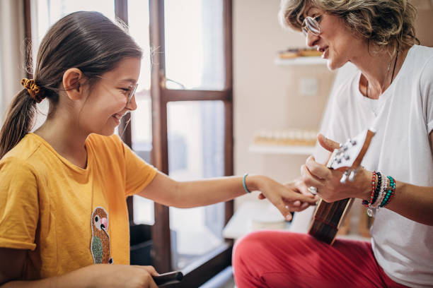 Girl with female teacher on music class learning to play guitar Two people, young girl on music class with female teacher, learning to play guitar. music therapy children stock pictures, royalty-free photos & images