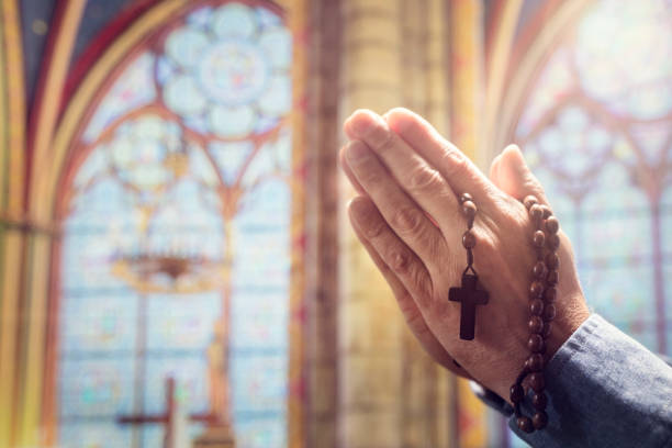 manos dobladas en oración en la iglesia con cuentas de rosario y cruz religiosa - rosario fotografías e imágenes de stock