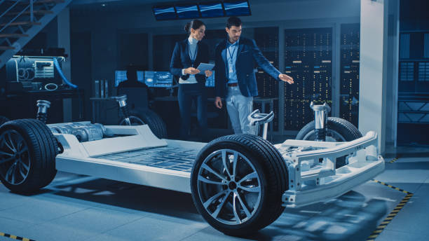 istock Female Chief Engineer Uses Tablet Computer, Introduces Autonomous Electric Car Concept to Important Investor, Describing Efficiency of Hybrid Engine. Vehicle Chassis Has Wheels, Engine and Battery 1270623276