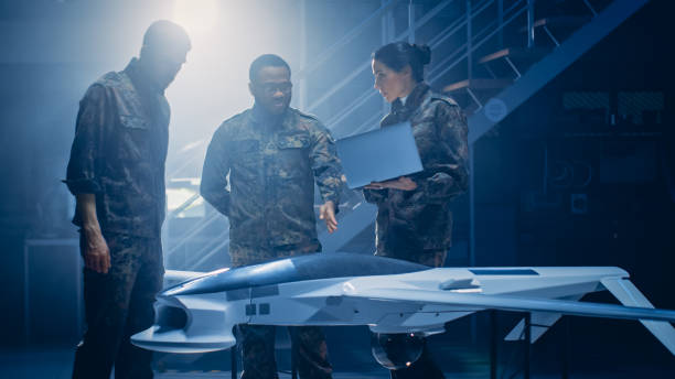istock Army Aerospace Engineers Work On Unmanned Aerial Vehicle / Drone. Uniformed Aviation Experts Talk, Using Laptop. Industrial Facility with Aircraft for: Surveillance, Warfare Tactics, Air Strike 1270623282