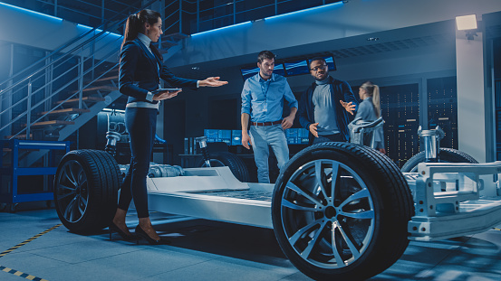 Equipo Internacional de Ingenieros de Diseño de Automóviles hablando y diseñando auto eléctrico autónomo. El chasis de la plataforma del vehículo tiene ruedas, motores, batería. Evolución de la eficiencia energética renovable limpia photo