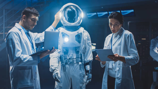 Diverse Team of Aerospace Scientists and Engineers Wearing White Coats have Discussion, Use Computers, Design New Space Suit Adapted for Galaxy Exploration and Travel. Constructing Astronaut Suit diverso equipo de científicos e ingenieros aeroespaciales que llevan abrigos blancos tienen discusión, uso de computadoras, diseño de nuevo traje espacial adaptado para la exploración de galaxias y viajes. construcción de traje de astronauta