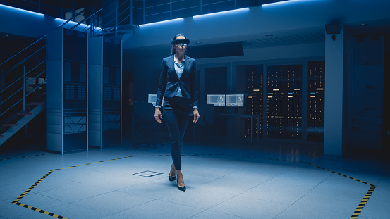 In 3D Content Creating Laboratory Stylish and Beautiful Female Engineer Wearing Professional Virtual Reality Headset Works and Gestures in Augmented Reality, Walking Through Facility