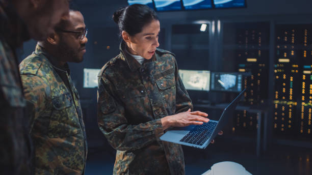국제 군인 팀이 일급 비밀 시설에서 회의를 하고 있으며, 여성 지도자는 남성 전문가와 노트북 컴퓨터 회담을 개최합니다. 전략군 회의에 제복을 입은 사람들 - men women laboratory indoors 뉴스 사진 이미지