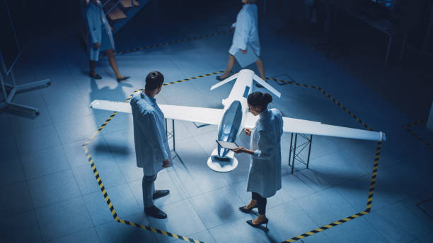 istock Two Aerospace Engineers Work On Unmanned Aerial Vehicle Drone Prototype. Aviation Scientists in White Coats Talking, Using Tablet Computer. Industrial Laboratory with Surveillance or Military Aircraft 1270623476