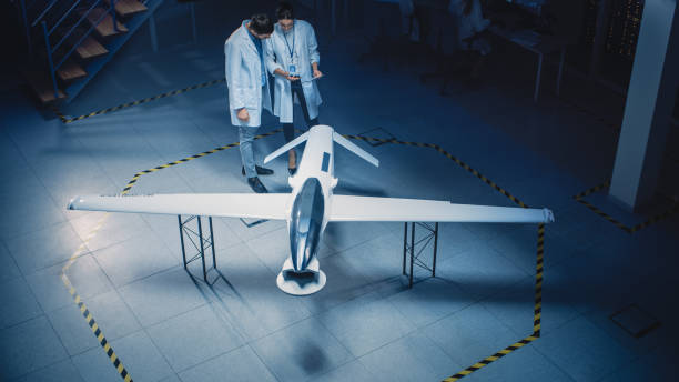 istock Two Aerospace Engineers Work On Unmanned Aerial Vehicle Drone Prototype. Aviation Scientists in White Coats Talking, Using Tablet Computer. Industrial Laboratory with Surveillance or Military Aircraft 1270623539
