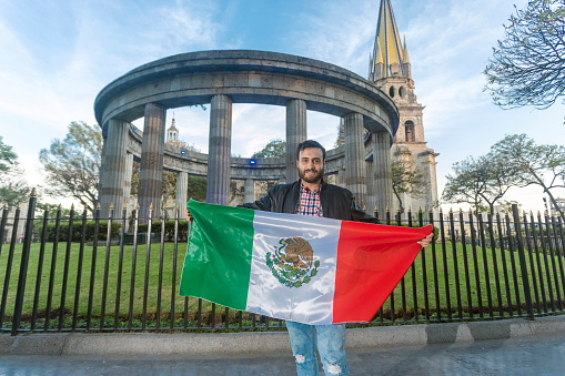 Young tourist with the flag of Mexico in the Rotunda and the Cathedral of Guadalajara, Jalisco, Mexico.