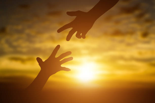Silhouette of giving a help hand, hope and support each other over sunset background. Concept of helping hands and develop a friendship.